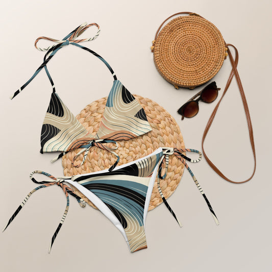All-over print recycled string bikini set with abstract colorful design, laid on a woven mat, includes removable padding and adjustable straps.