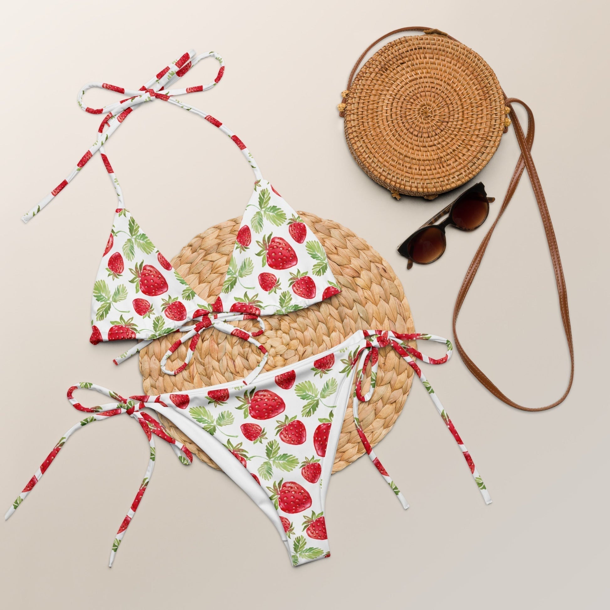 Strawberry pattern all-over print recycled string bikini set on display with straw bag and sunglasses.