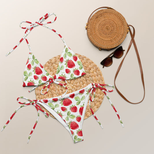 Strawberry pattern all-over print recycled string bikini set on display with straw bag and sunglasses.
