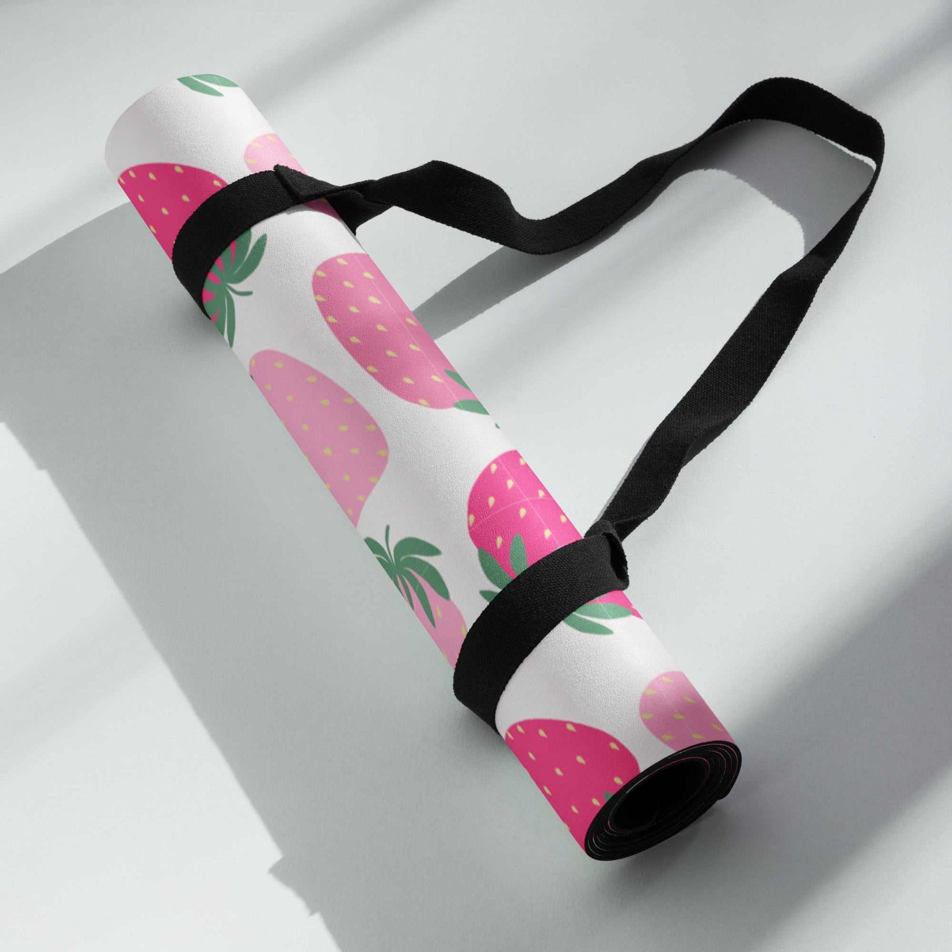 Rolled pink and white yoga mat with strawberry design and black carry strap.